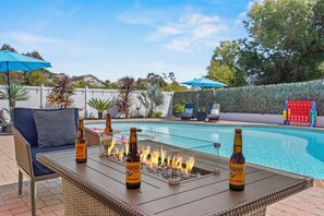 A poolside area with a fire feature, lounge chairs, and a table with bottles.