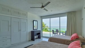 A bedroom with two beds, a wardrobe, a desk, and a balcony with a view of the ocean. - Casa Nazul  -  Yucatan Home Rentals (Chicxulub Puerto)