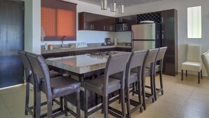 A modern kitchen with a central island, dark cabinetry, stainless steel appliances, and a seating area with bar stools. - Casa Nazul  -  Yucatan Home Rentals (Chicxulub Puerto)