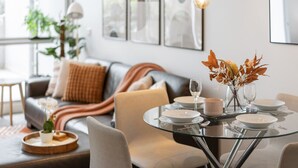 A modern dining area with a glass table set for two, a sofa in the background, and a vase with flowers on the table. - Ultimate Comfort Gem in St Kilda  ⭐⭐⭐⭐⭐ (St Kilda)