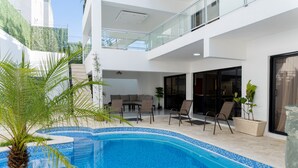 Ein moderner Poolbereich im Freien mit Glasbrüstung, Liegestühlen und einer Palme.