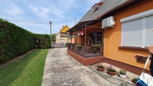 A residential building with a covered porch, potted plants, and an air conditioning unit. - Holiday apartment with wifi and parking (Balatonboglár)
