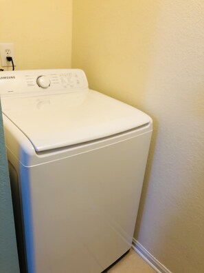 Een witte Samsung wasmachine in een wasserij met een effen gele muur en een blauwe deur.