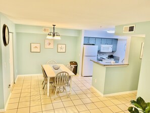 A dining area with a table and chairs, a kitchen with appliances, and a light blue wall with framed pictures. - Gorgeous 3 bed 2 bath condo with pool near beach (DESTIN)