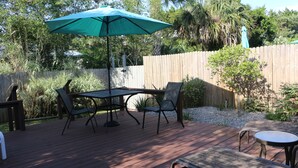 Una terraza de madera con una mesa, sillas, un paraguas verde y una valla de madera.