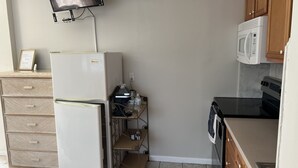 A compact kitchen with a refrigerator, microwave, oven, and a TV mounted on the wall.
