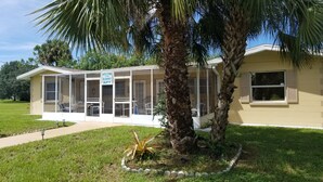 A single-story building with a covered porch, a 'Welcome to Sunny APT' sign, and a palm tree in the foreground.