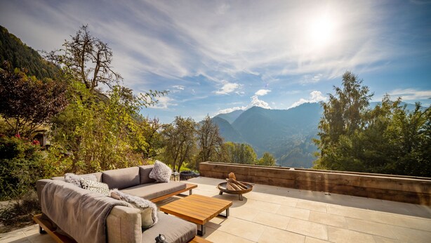 Un área de estar al aire libre con un sofá, una mesa de centro y una chimenea, con vistas a un paisaje montañoso.