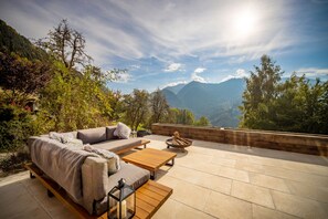 An outdoor seating area with a sofa, coffee table, and a fire pit, overlooking a mountainous landscape. - Gamelbarn is a beautiful luxury chalet with hot tub and stunning mountain views (Saint-Jean-d'Aulps)