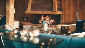 Una habitación acogedora con chimenea, una mesa de vidrio con una botella y copas, y un sofá azul.