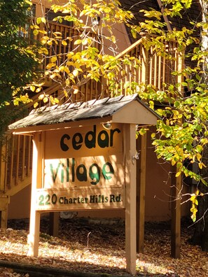Un letrero de madera con el texto 'cedar village' y '220 charter hills rd'.