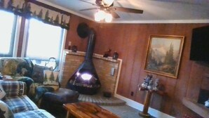 A cozy living room with a fireplace, a ceiling fan, and a large painting on the wall. - Cedar Village Condo A5, Beech Mountain, NC (Beech Mountain)