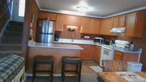 A compact kitchen with wooden cabinets, a microwave, a stove, and two bar stools.