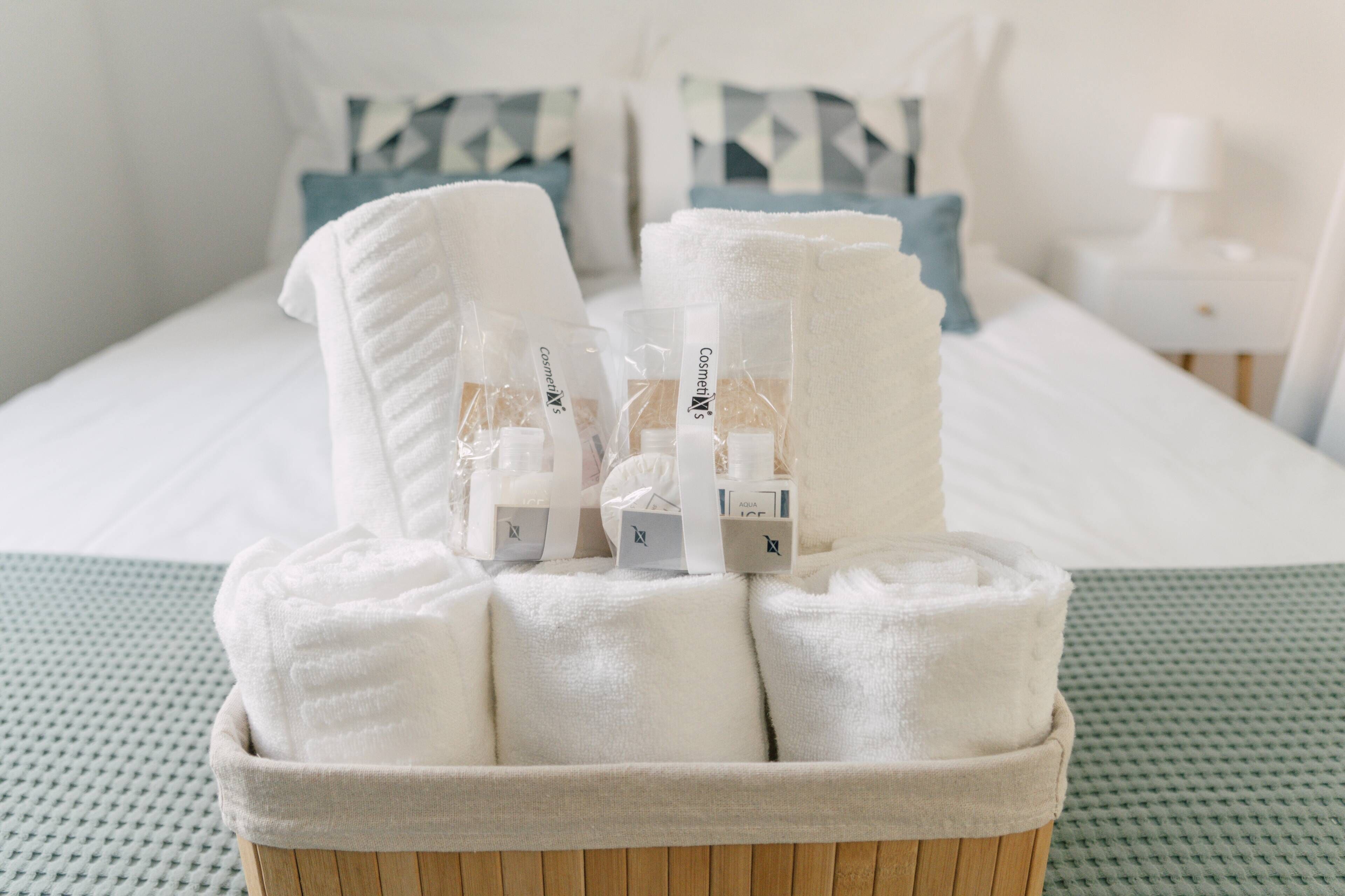 Netjes opgevouwen handdoeken en toiletartikelen in een houten mandje op een bed met een groen geweven sprei.