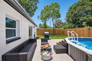 A backyard with a swimming pool, a barbecue grill, and outdoor seating.