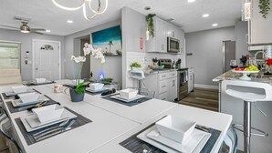 Een moderne keuken met witte kasten, roestvrijstalen apparatuur en een eethoek voor zes personen, compleet met een centraal kookeiland.