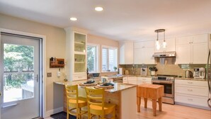 A modern kitchen with white cabinets, a central island with stools, and a large window providing natural light. - Peaceful retreat plus Dog Friendly! (Wellfleet)