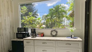 A kitchen with a window view of palm trees, a microwave, a coffee maker, and a clock on the counter. - Cozy Luxury Suite In The Heart Of Fort Myers Close To Everything! (Fort Myers)