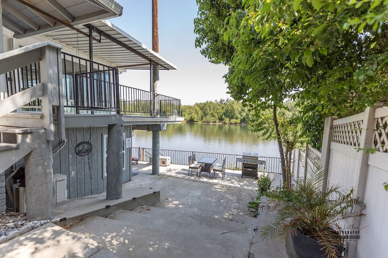 A lakeside patio with outdoor furniture, a grill, and a view of the lake.