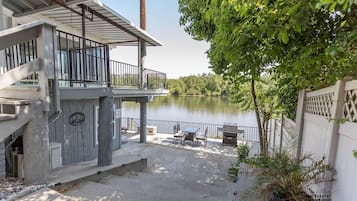A lakeside patio with outdoor furniture, a grill, and a view of the lake.