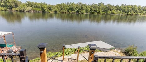 Un escalier en bois mène à une jetée où est amarré un bateau, et offre une vue sur un lac paisible, avec une végétation luxuriante en arrière-plan.