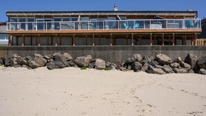 Un immeuble situé en bord de mer, doté d’un balcon, de grandes fenêtres et d’une terrasse en bois.