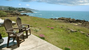 A patio with two chairs and a table overlooking a coastal view with rocks and the ocean. - Coastal Breakers Condo, Ocean Patio, BBQ & Pool (Depoe Bay)