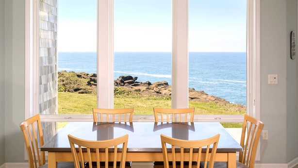A dining area with a table and chairs, large windows with a view of the ocean and rocks. - Paradise Regained Condo, Whale Watching & Pool (Depoe Bay)