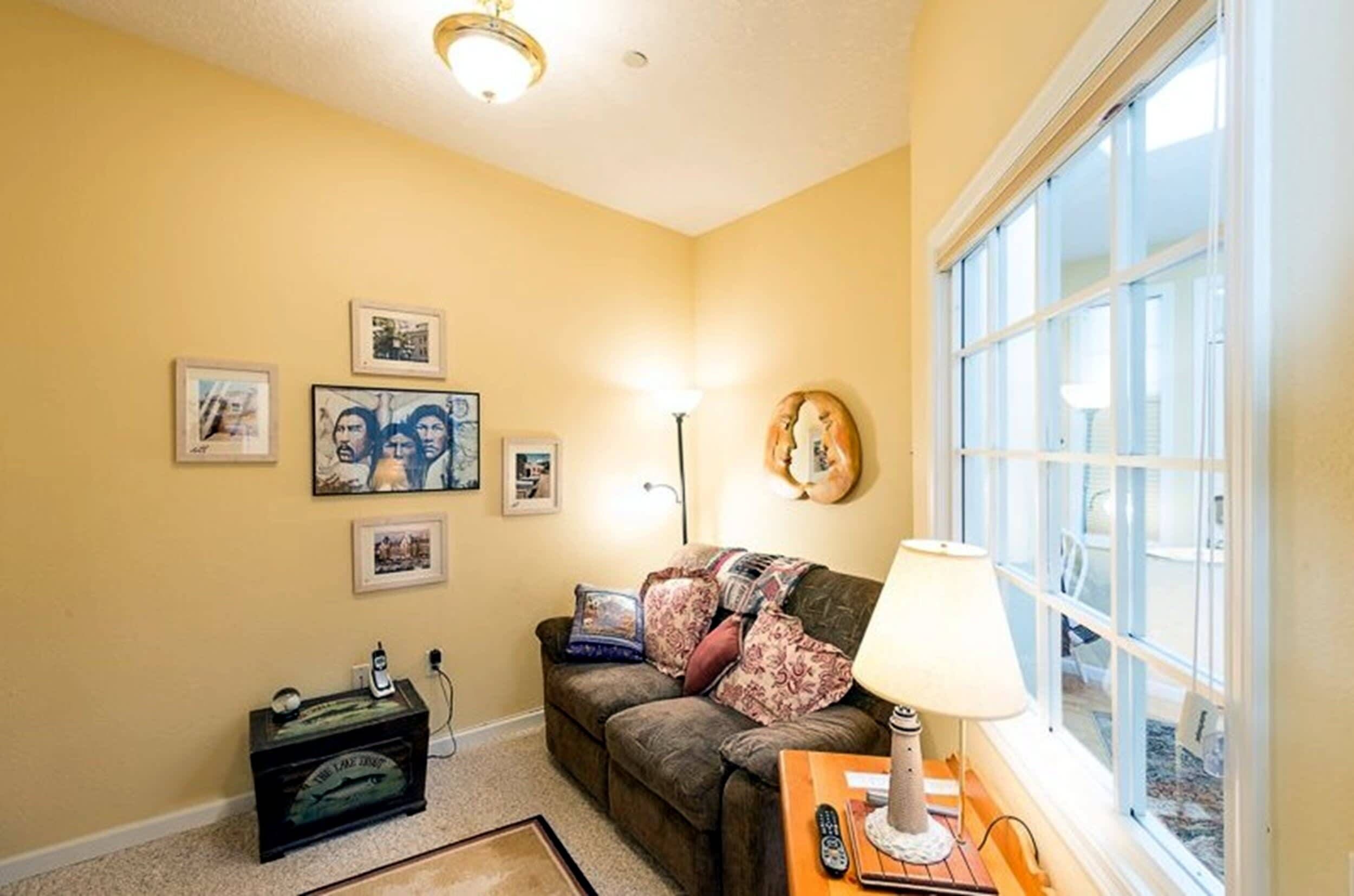 A living room with a couch, a lamp, a window, and wall art.