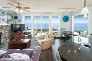 Un salon doté d’une cheminée en pierre, d’un téléviseur, d’un canapé, d’une table basse et offrant une vue sur l’océan grâce à de grandes portes vitrées.