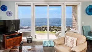 Ein Wohnzimmer mit einem großen Fernseher, einem Ledersofa und Meerblick durch Glastüren.