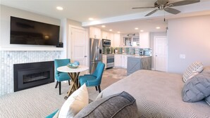 A modern living room with a fireplace, a TV mounted on the wall, and a kitchen in the background.