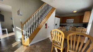A dining area with a wooden staircase, a kitchen in the background, and a 'BEACH' sign on the wall. - Jersey Shore - Summer 2025 - Lavallette - Sleeps up to 8! (Lavallette)