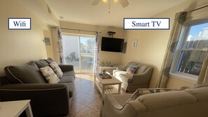 A living room with a sofa, a coffee table, and a TV. There is a sign indicating WiFi and a sign indicating a Smart TV. - Jersey Shore - Summer 2025 - Lavallette - Sleeps up to 8! (Lavallette)