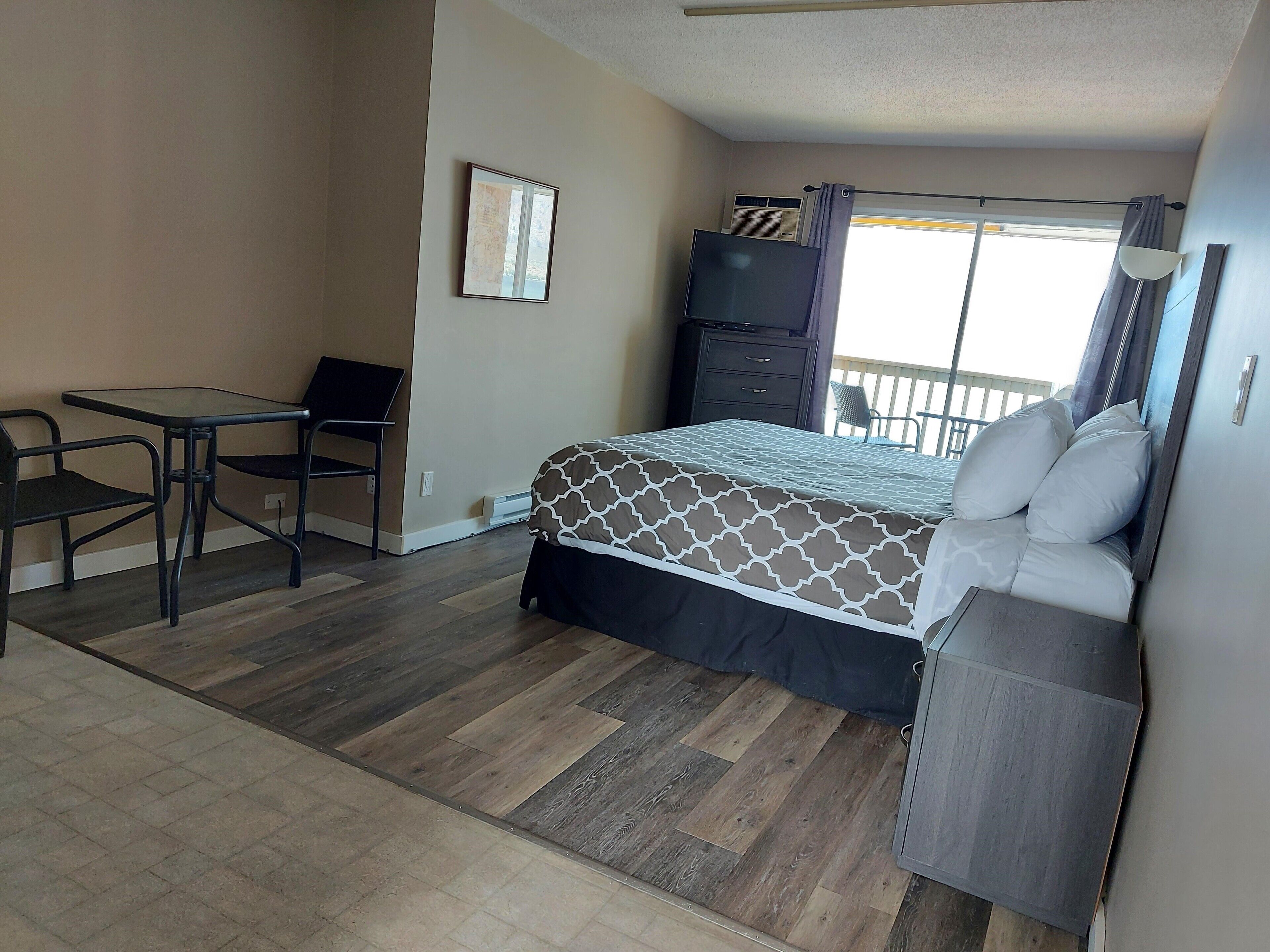 Un dormitorio con cama, escritorio y silla. Se ve una ventana con cortinas y vistas al exterior.