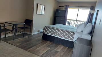 Un dormitorio con cama, escritorio y silla. Se ve una ventana con cortinas y vistas al exterior.