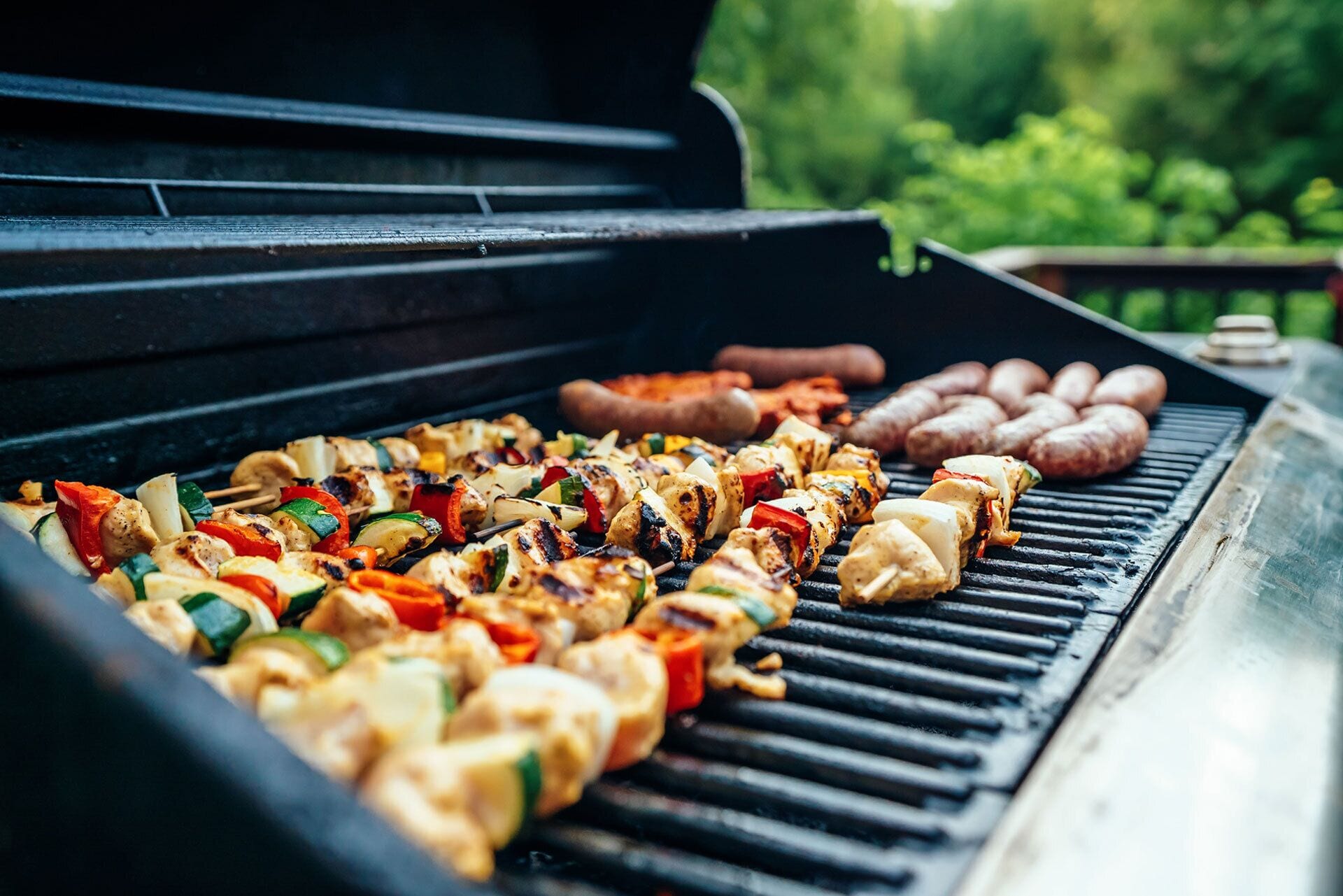 Un barbecue avec des brochettes de poulet et de légumes, des saucisses et d’autres viandes.