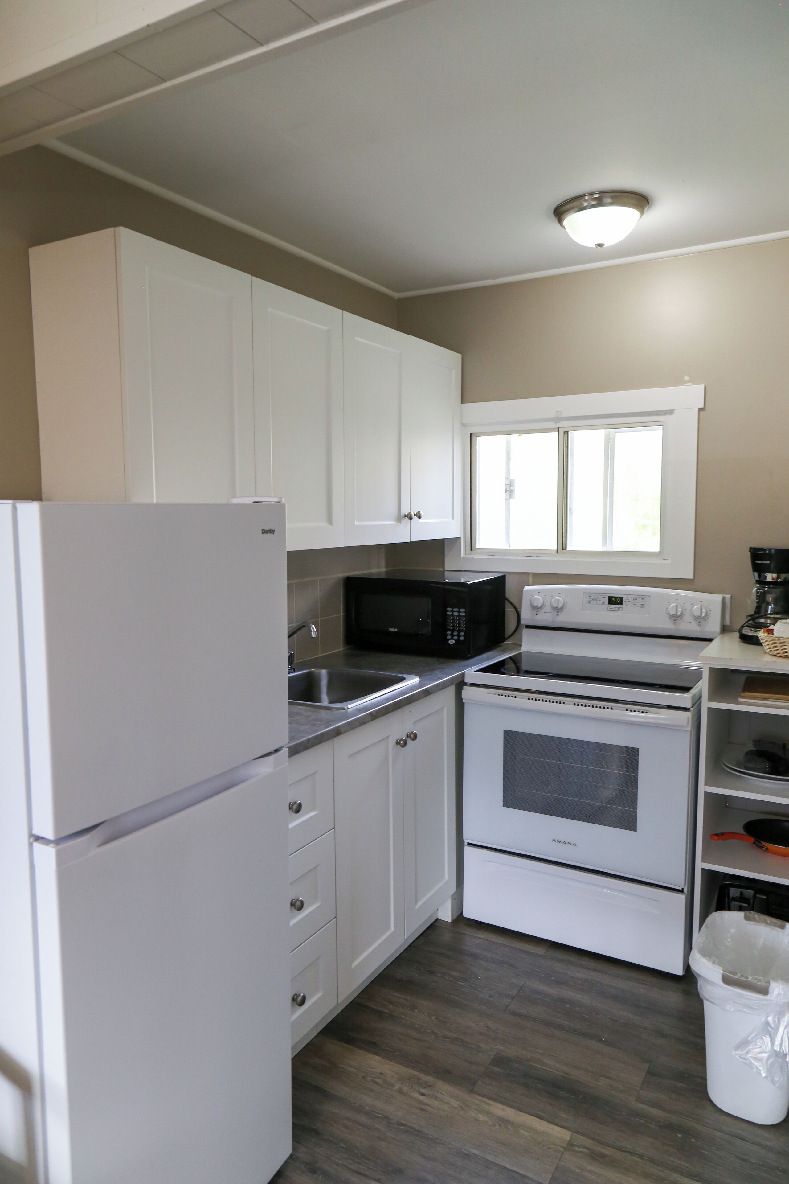 A compact kitchen with white cabinets, a refrigerator, a microwave, an oven, and a window above the sink.