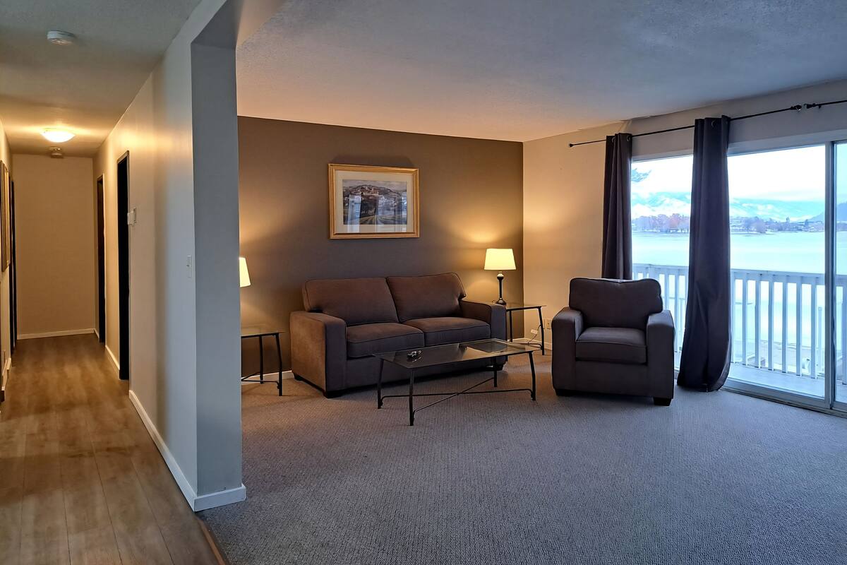 A hotel room with a sofa, armchair, and a view of a body of water.