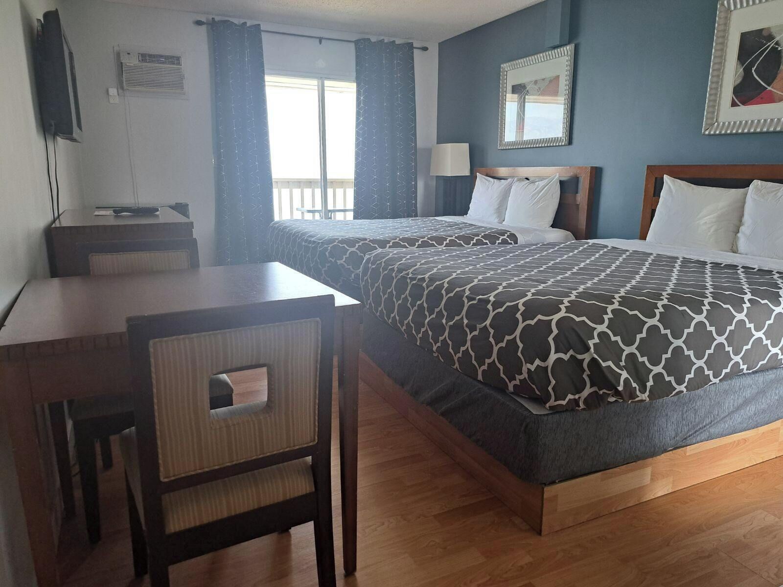 Una habitación de hotel con cama, escritorio, silla, televisor, ventana con cortinas y espejo en la pared.