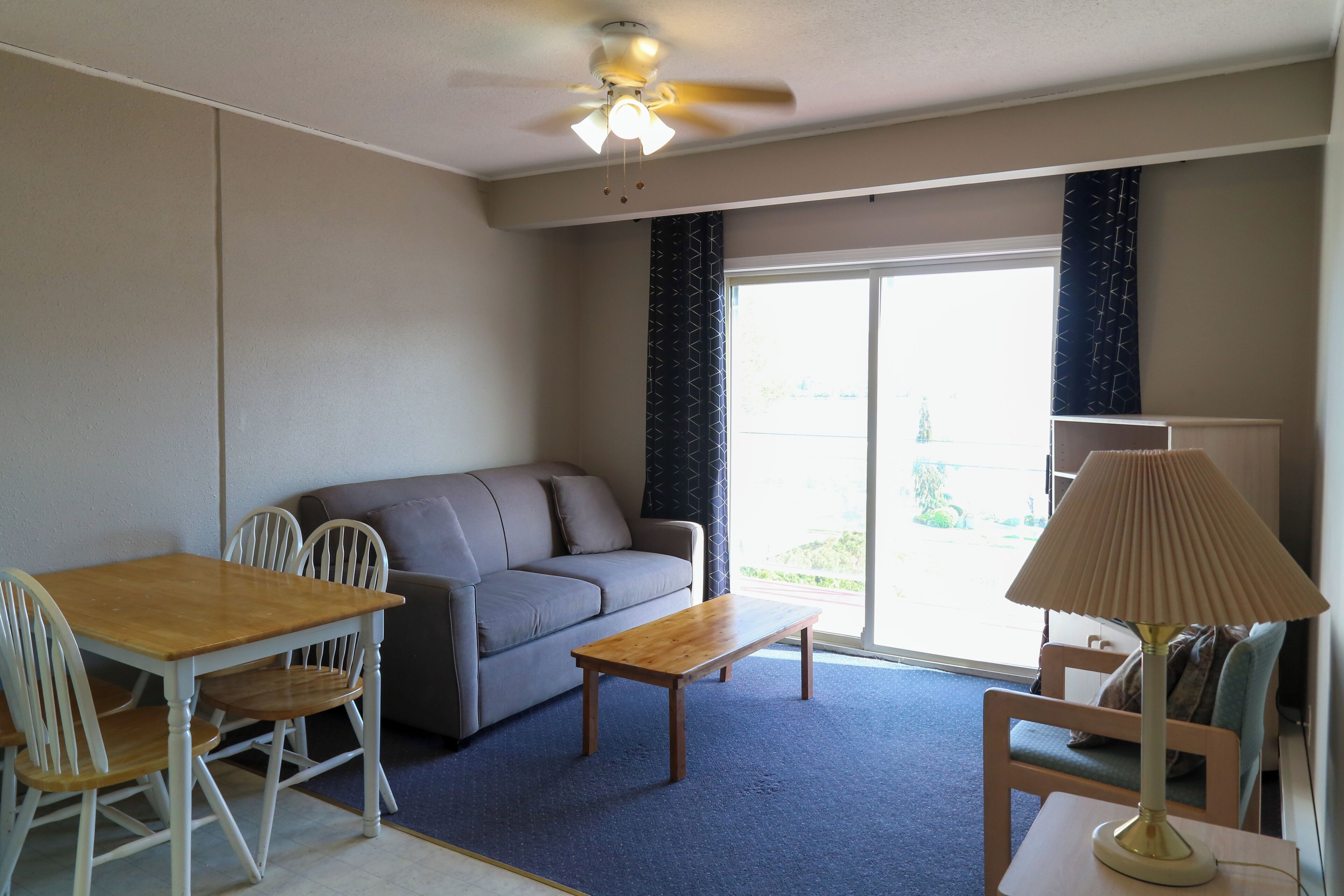 A room with a ceiling fan, a sofa, a wooden table, and a lamp.