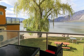A terrace with a view of a lake, a willow tree, and a mountain in the background.