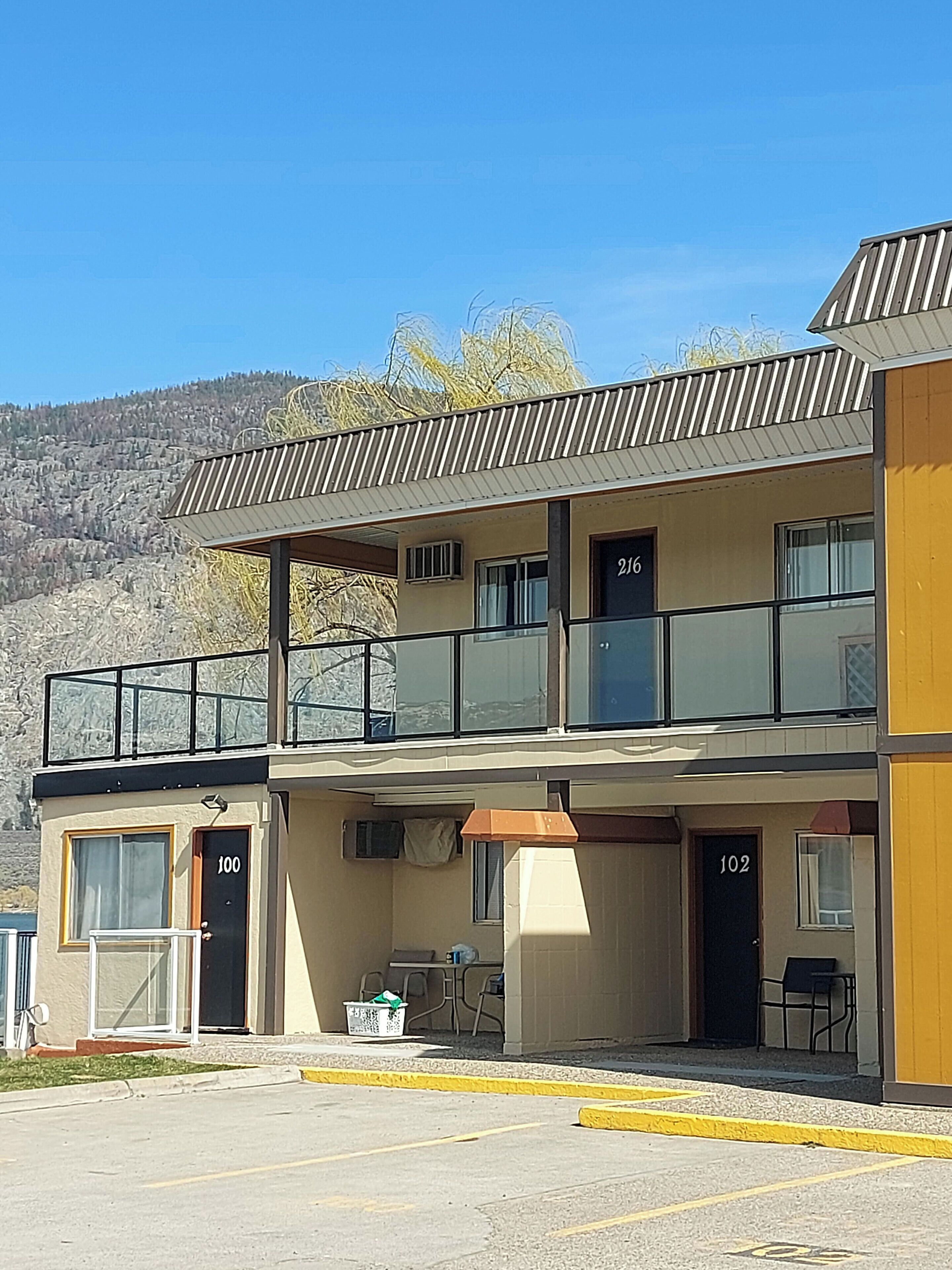 A two-story building with numbered doors, a balcony, and a parking lot in front.