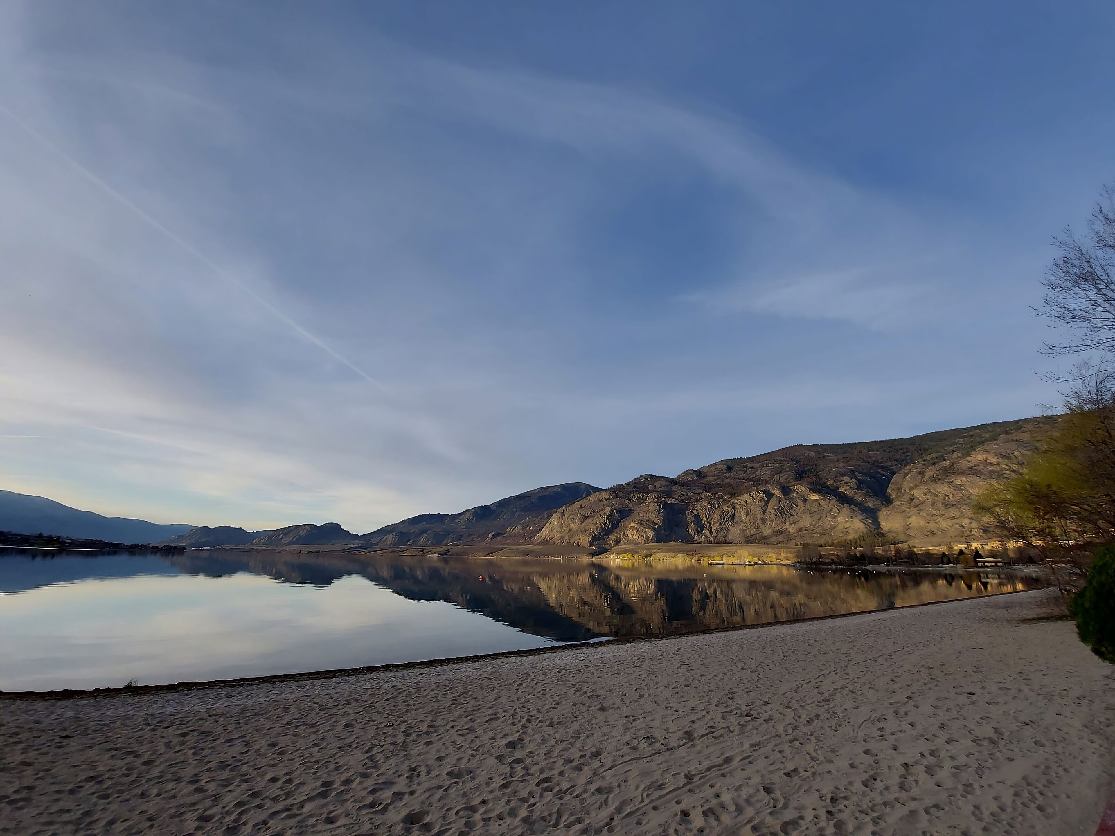 Un lago tranquilo con una playa arenosa y montañas rocosas al fondo.