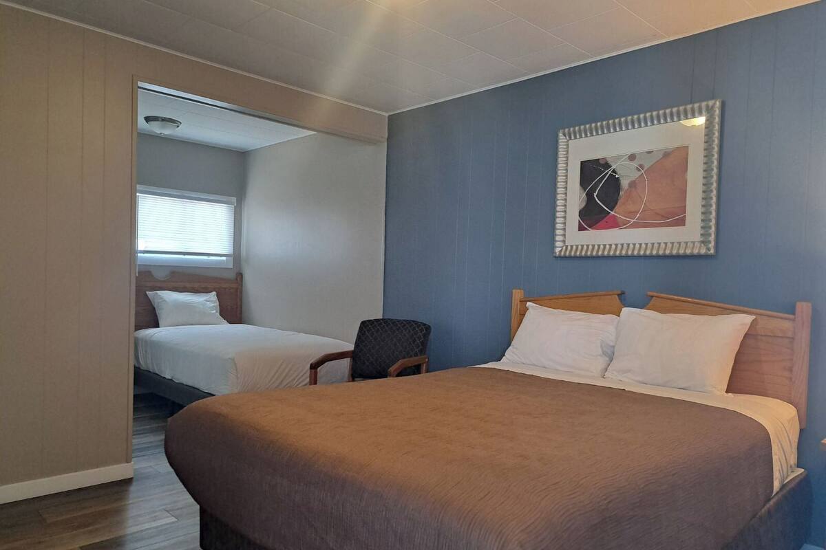 A hotel room with a large bed, a smaller bed in the background, a chair, and a framed picture on the wall.