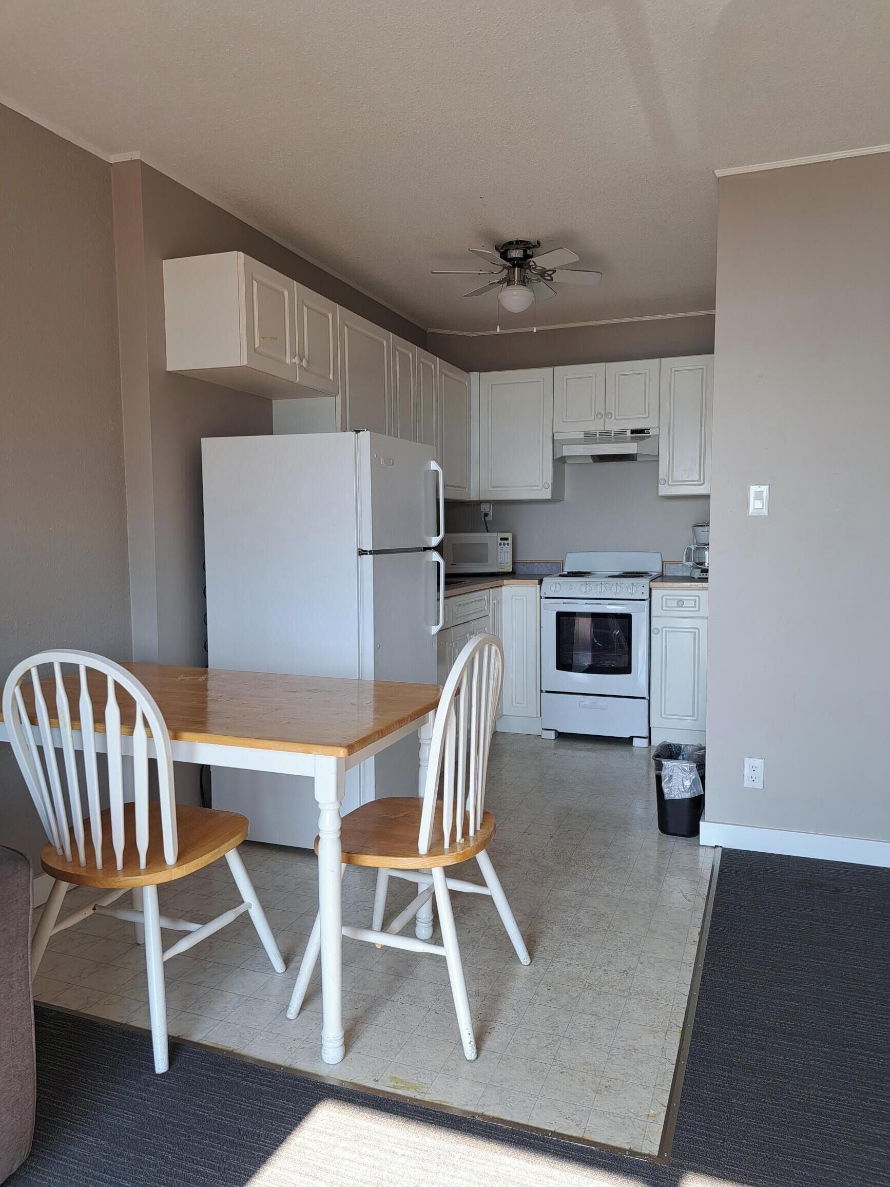 A compact kitchen with white cabinets, a microwave, a stove, and a ceiling fan.