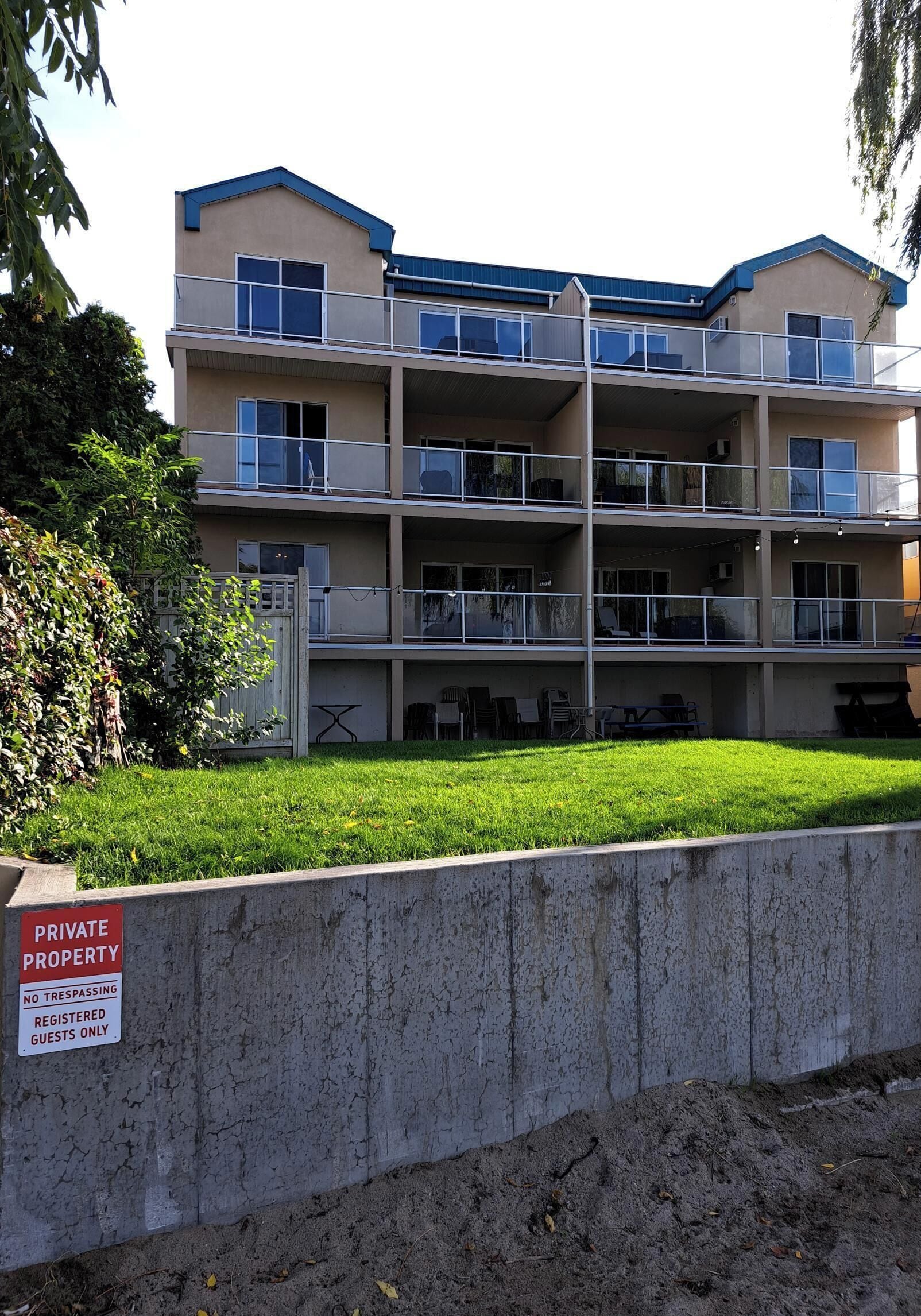 A multi-story residential building with balconies, a grassy front yard, and a 'Private Property' sign.