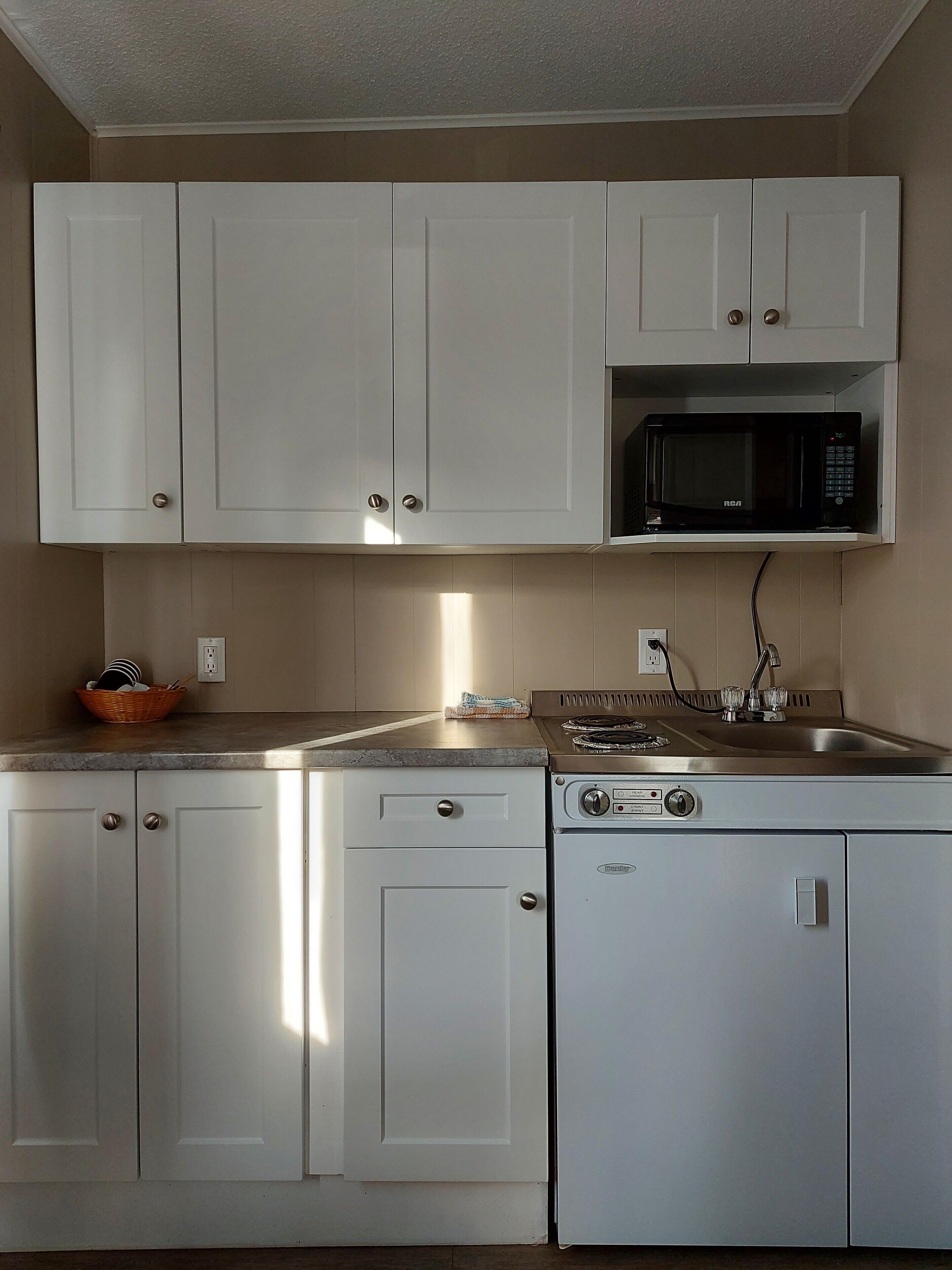 Una cocina con armarios blancos, microondas, estufa y fregadero.