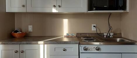 Una cocina con armarios blancos, microondas, estufa y fregadero.
