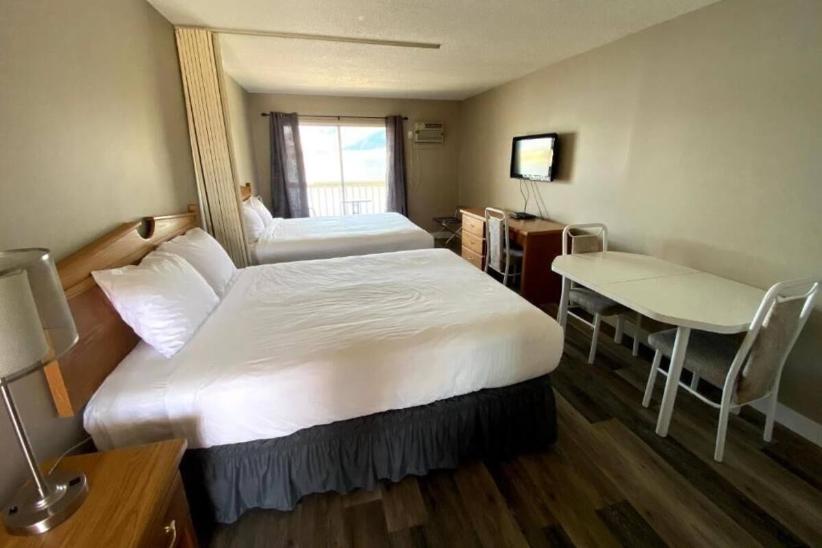 A hotel room with two beds, a desk, a chair, a television, and a window with curtains.